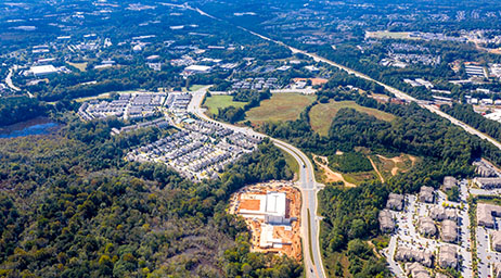 Вид с высоты птичьего полета на г. Джонс-Крик, штат Джорджия, с дороги, проходящей через застроенные районы, окруженные деревьями