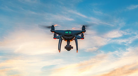 Um drone preto com luzes vermelhas voando através de um céu azul e nublado