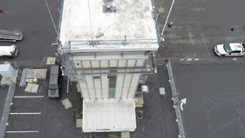 An aerial view of a white, multistory control tower surrounded by asphalt