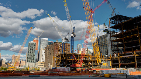 Chantier de construction d’un gratte-ciel avec plusieurs grues de grande taille sous un ciel bleu parsemé de quelques nuages