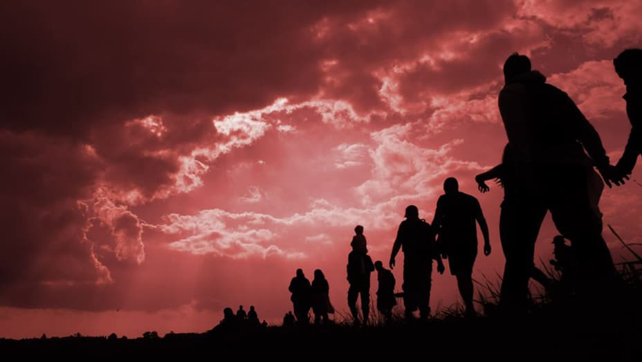 Line of silhouetted people moving right to left against a cloudy deep red sky