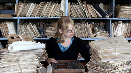 A person sitting at a desk surrounded by stacks of files and papers 