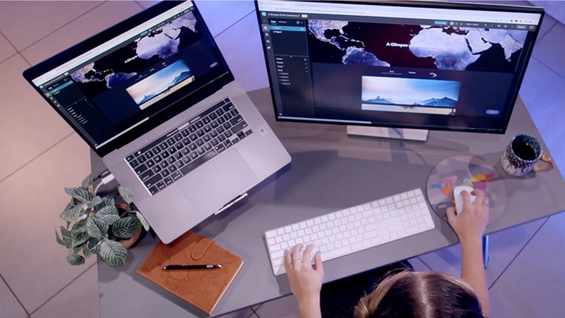 An overhead view of a person using a computer and monitor with displays of a map of the continents 