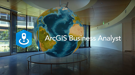 Espace de bureau moderne avec un large globe suspendu au centre, recouvert par le nom et le logo d’ArcGIS Business Analyst en blanc