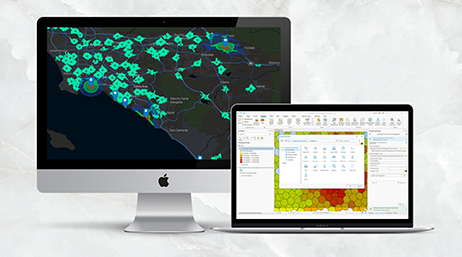 Um computador desktop com um mapa na tela e um laptop com uma tela exibindo uma interface de software