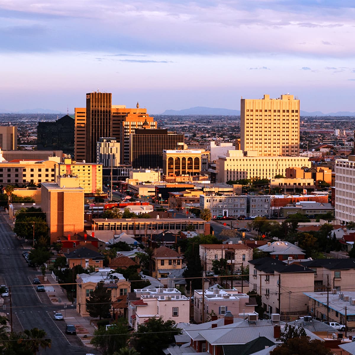 An aerial view of a large city at dawn with low-rise buildings in the foreground, against a vibrant blue and purple sky.