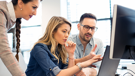 Three employees talking and looking at a computer monitor 