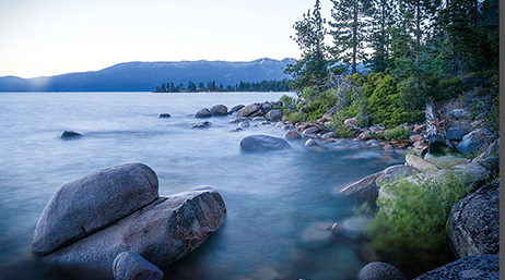 A lake in Placer County with green trees, rocks, and a mountain in the distance