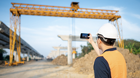 Мобильный сотрудник в белой каске и оранжевом жилете фотографирует строительную площадку