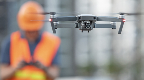Un dron volando en el aire con un enfoque nítido con un trabajador móvil que lleva un casco naranja y un chaleco al fondo