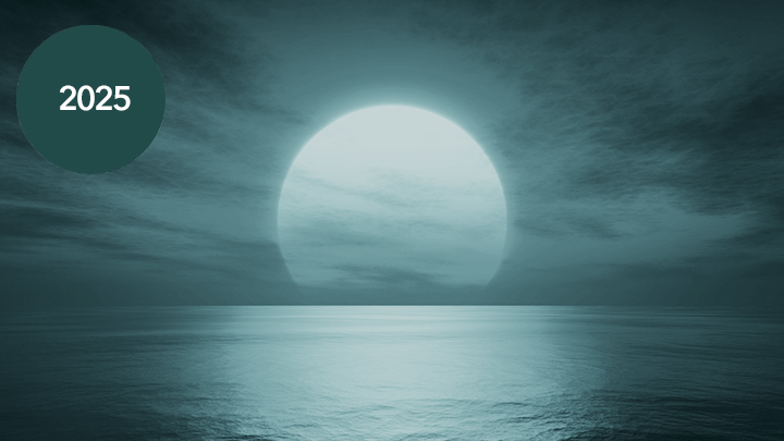 A blue image of the sun in a cloudy sky setting over an ocean