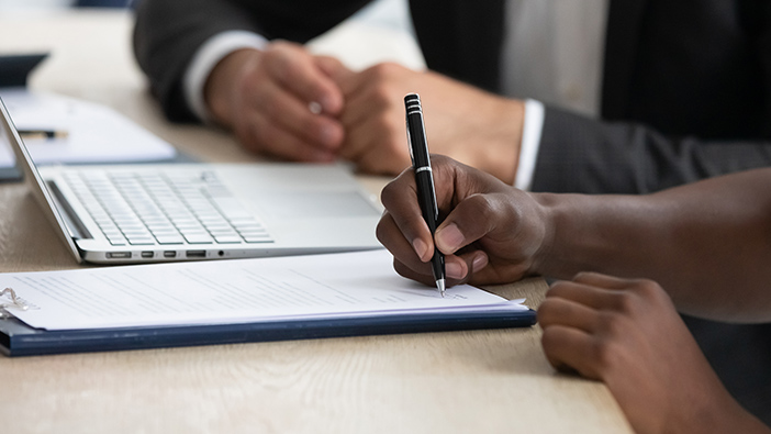 Two people signing a contract at a desk next to an open laptop