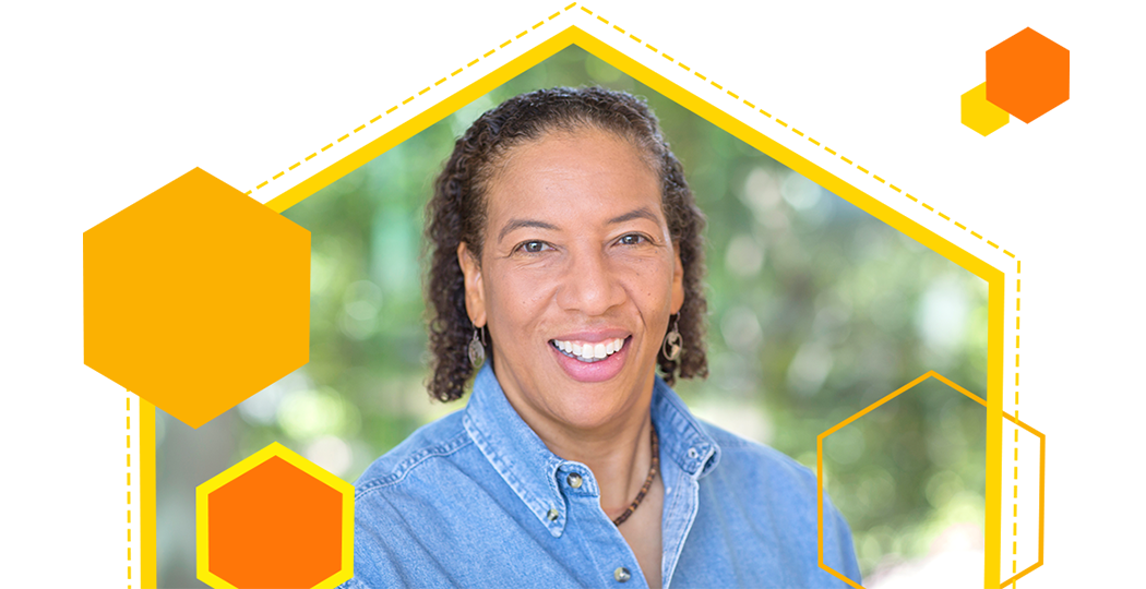 Portrait of Dawn Wright smiling in a denim collared shirt with a soft-focus background of sun-dappled trees