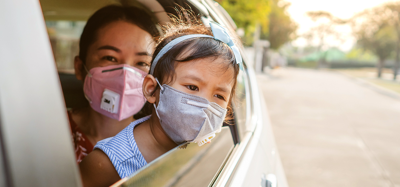Eine Frau mit einem kleinen Kind, die beide Maske tragen, in einem Auto