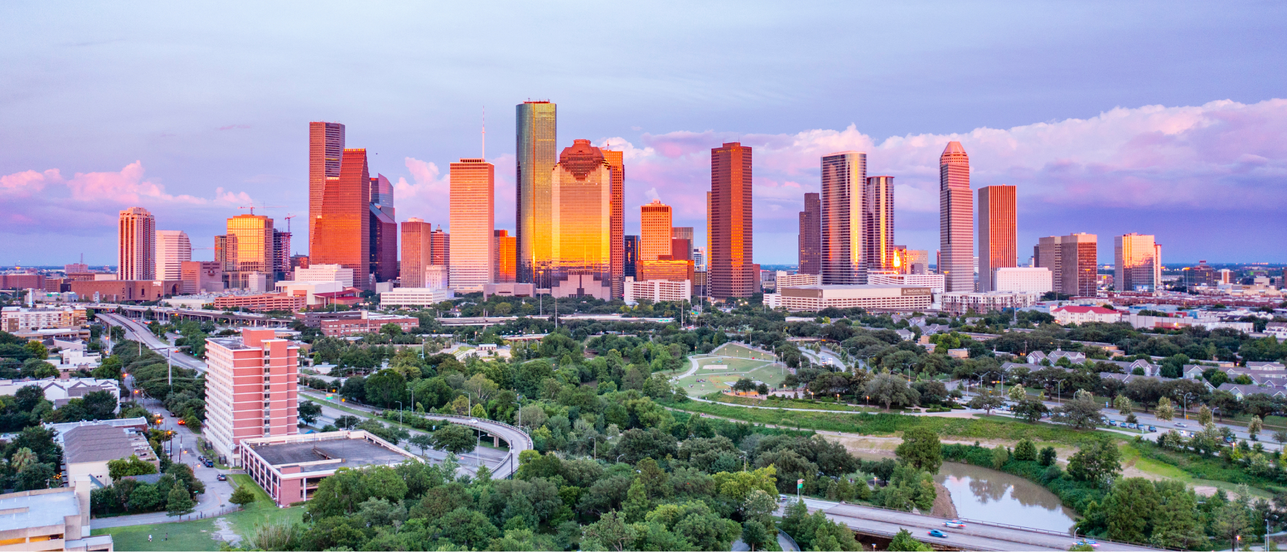 A panoramic image of a modern city with many mirrored skyscrapers reflecting warm sunrise colors, surrounded by a prospering cityscape filled with green trees and parks