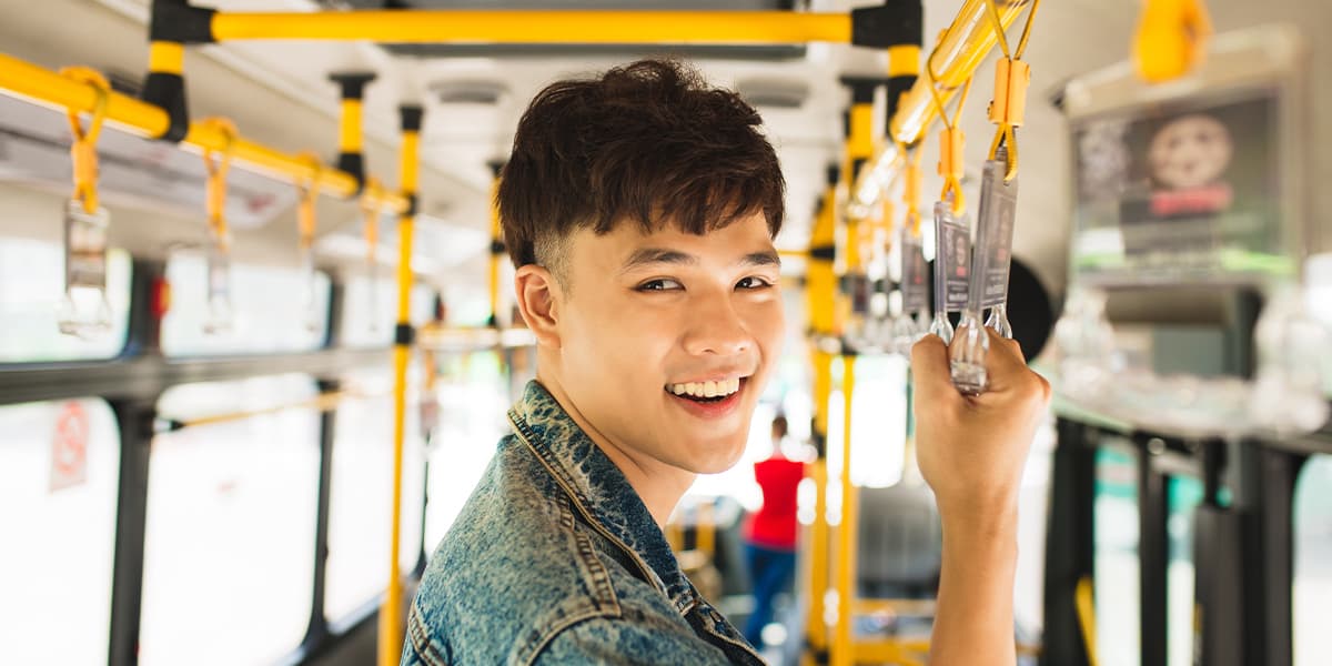 Un joven contento tomando el transporte público, de pie en un autobús