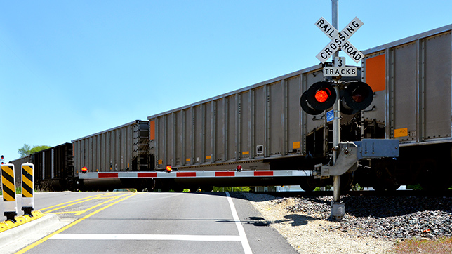 Tren de mercancías que cruza una carretera por un cruce ferroviario con las barreras bajadas y la luz roja encendida