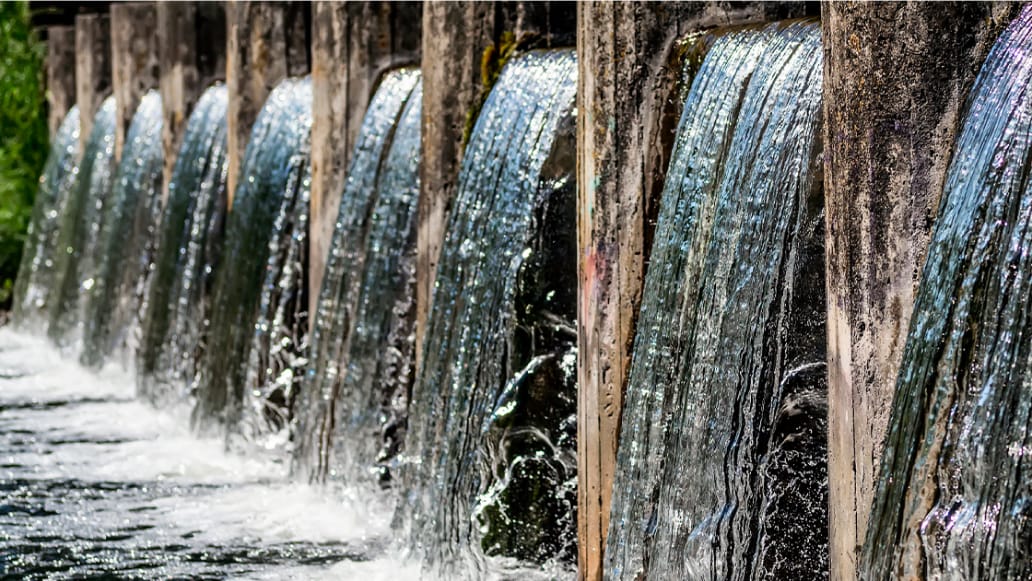 Closeup view of row of sluice gates with water pouring out into a dark river