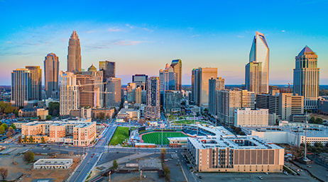 A sprawling modern city with a stadium in the center under a calm blue and pink sunrise sky