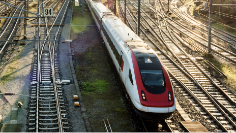 قطار ركاب باللون الأبيض والأحمر يتحرك عبر منطقة تبديل سكك حديدية مع وجود العديد من المسارات في صف متتالي