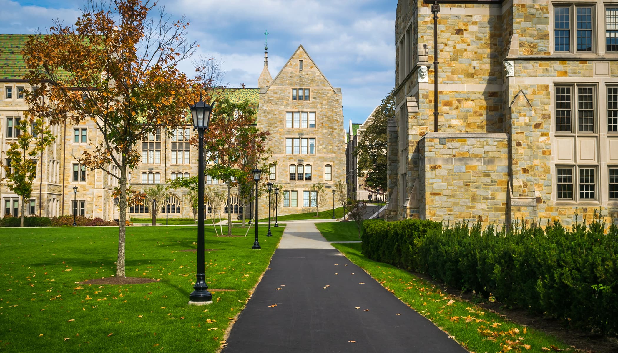 Stone and brick buildings with a walkway passing through, surrounded by a tree-lined lawn.