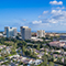 Aerial image of a sprawling college campus nestled between suburban tree-lined neighborhoods and a spread of skyscrapers under a cloud-swept blue sky