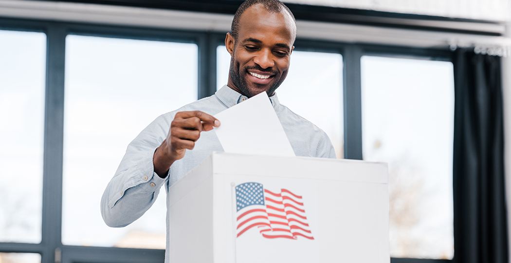 A person putting their ballot into a ballot collection box that has an American flag on the front