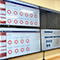 Four large TV screens displaying metrics and maps near a whiteboard in a brightly lit office