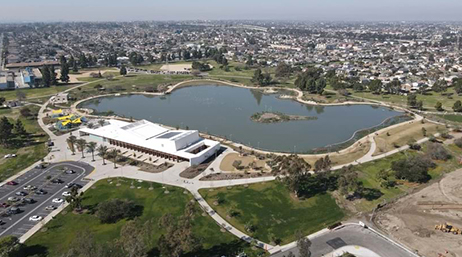 An aerial view of Magic Johnson Park in Los Angeles, with green tree-dotted fields surrounding a large manmade lake