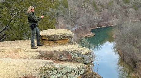 A person wearing casual hiking gear taking a picture of Harpeth River from atop a stone outcropping