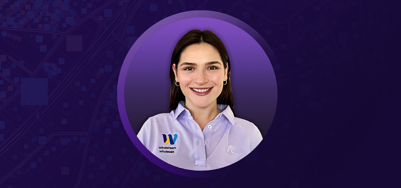Natalie May wearing a purple collared shirt and smiling overlaid on a purple background 