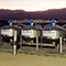 A row of five large, industrial water filtration tanks on a concrete pad in a desert landscape