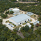 An aerial view of an industrial plant surrounded by trees near a highway and a body of water