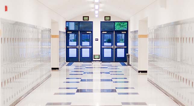 Jasno oświetlony korytarz szkoły średniej z czystymi białymi schowkami po obu stronach i dwiema parami w błękitnych drzwi na końcu