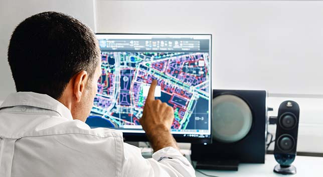 白い襟付きのシャツを着た人物がデスクトップ コンピューターを使用して、青、白、紫のデジタル都市マップを見ている様子