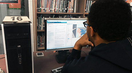Учащийся, использующий настольную компьютерную станцию для доступа к цифровой карте и данным в школьной библиотеке