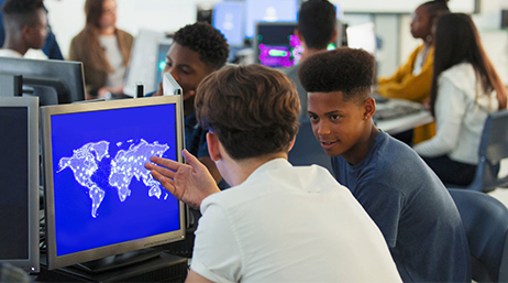 Students talking to each other and working on desktop computers in a computer lab