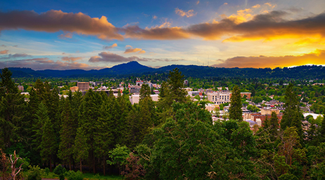 A town surrounded by evergreen trees and a mountain range at sunset