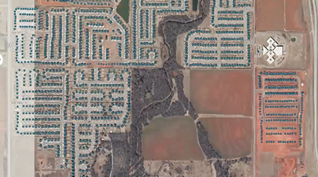 An aerial image of a large housing tract full of blue-roofed homes set in reddish brown areas of land