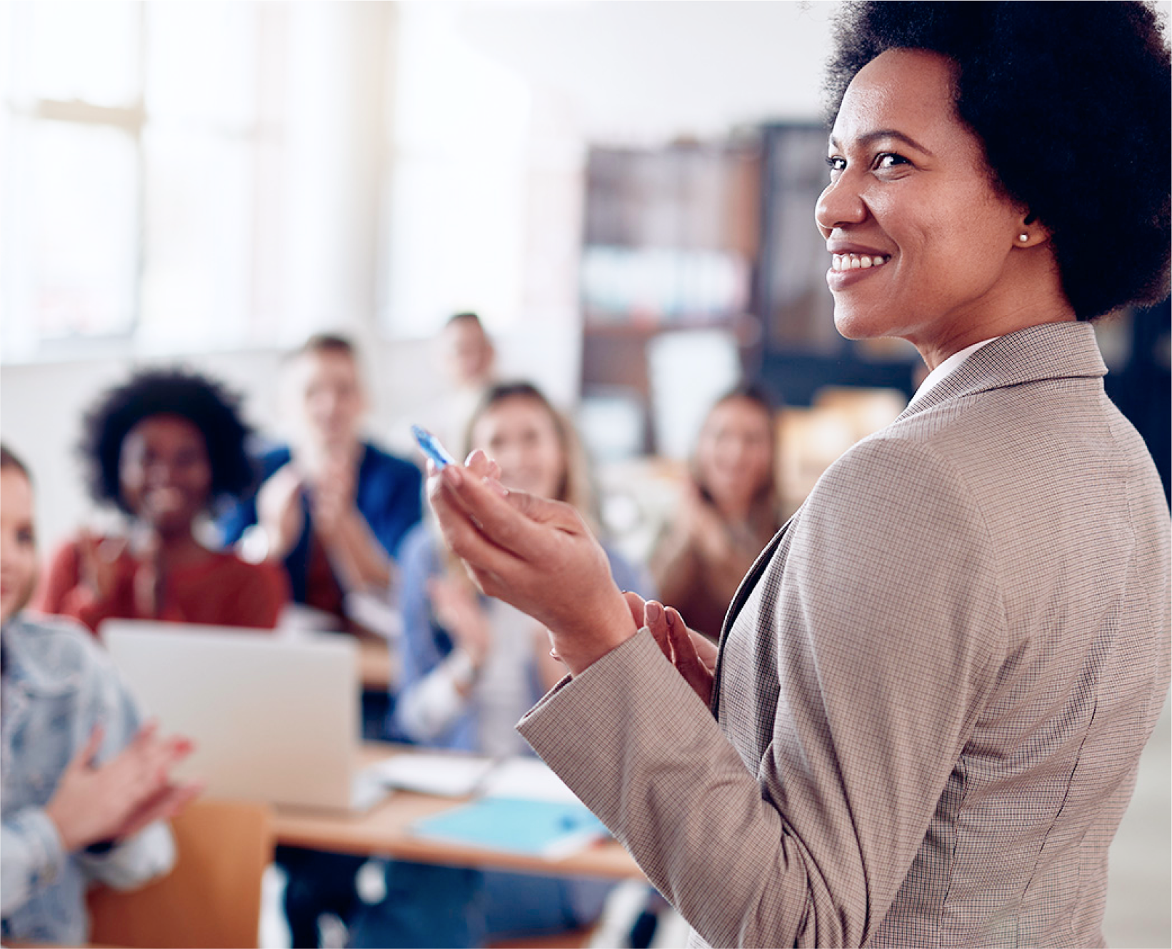 A teacher smiling and pointing off to the side in a classroom with students