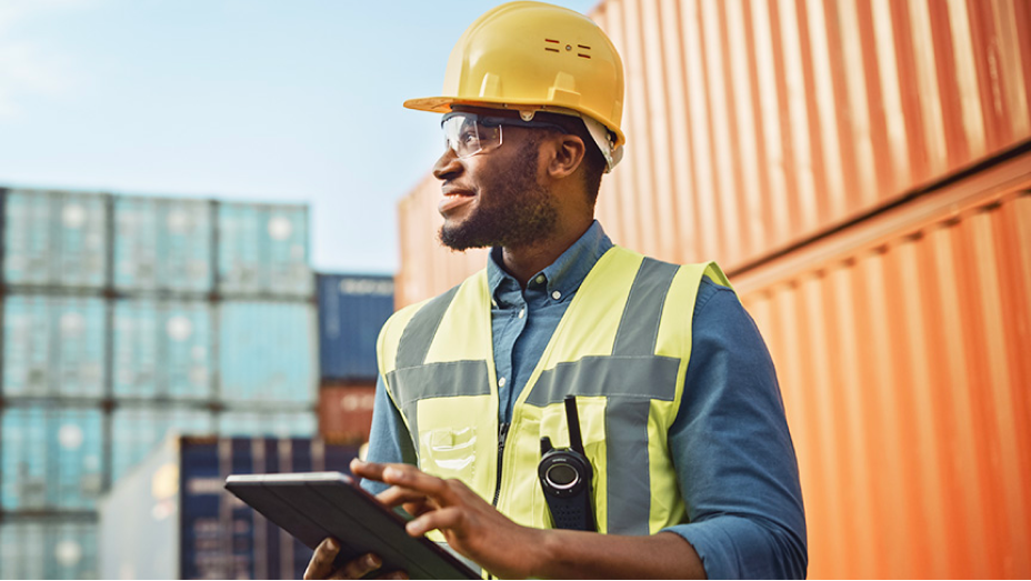 Person standing outside using GIS on a tablet computer and wearing a hard hat