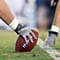 Side view of a center’s hand and arm holding a football on the line of scrimmage before play starts