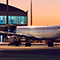 A jet airplane parked at an airline gate at dusk with a jetway to the left