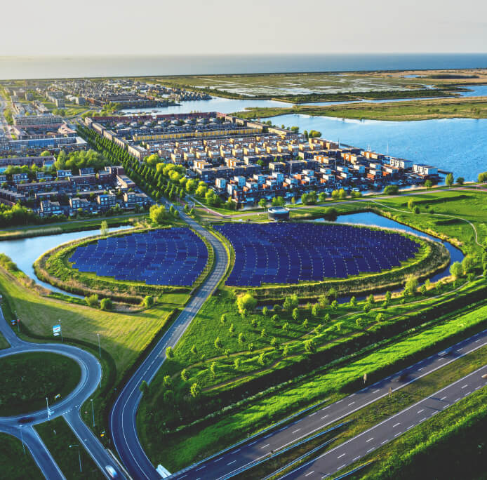 Vista aérea de una carretera que atraviesa un parque solar y una zona residencial cerca del agua.