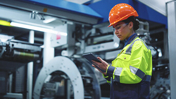 A woman in a hardhat holding a tablet computer next to a large machine
