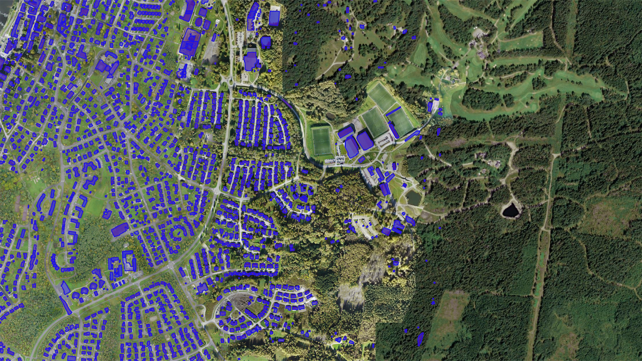 Aerial imagery of a suburban area with a dense forest to the right. The rooftops are highlighted in blue, indicating potential for solar panel installations.