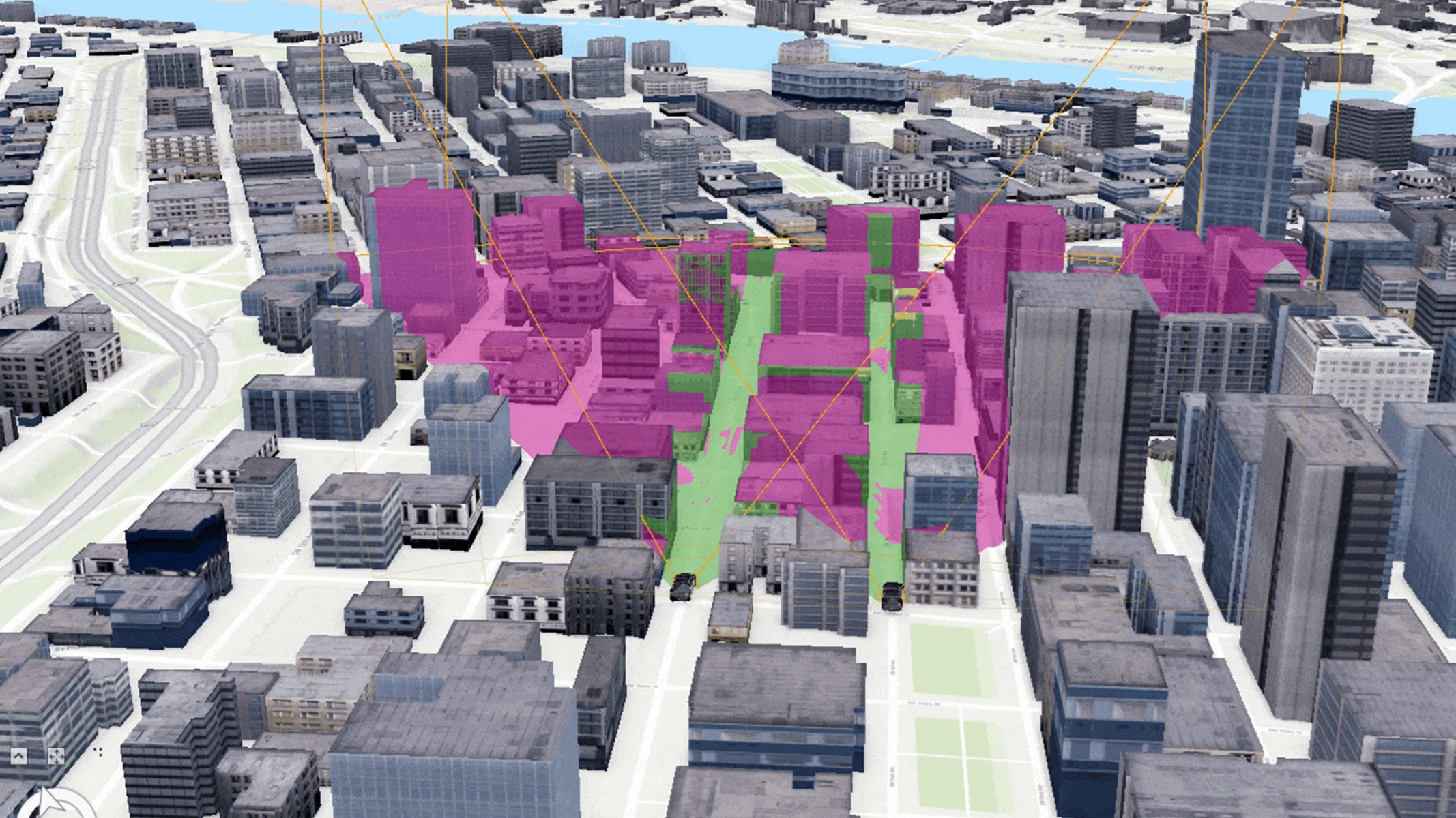 A 3D model of a city center. Several buildings are highlighted in shades of pink and green, indicating zones or areas of interest within the city.