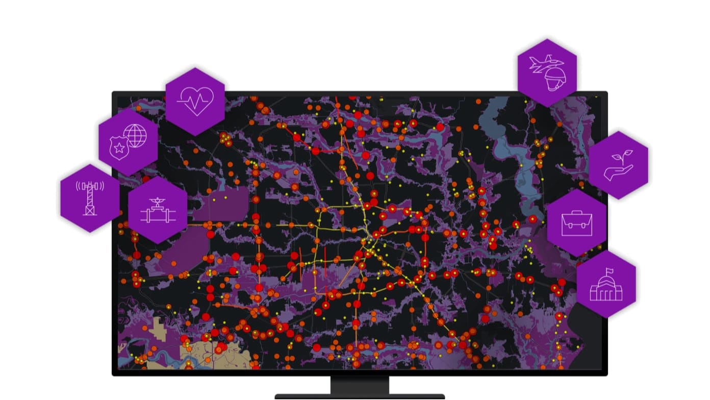 A computer monitor displaying a map with areas shaded in purple and many red dots overlaid with icons for ArcGIS Solutions