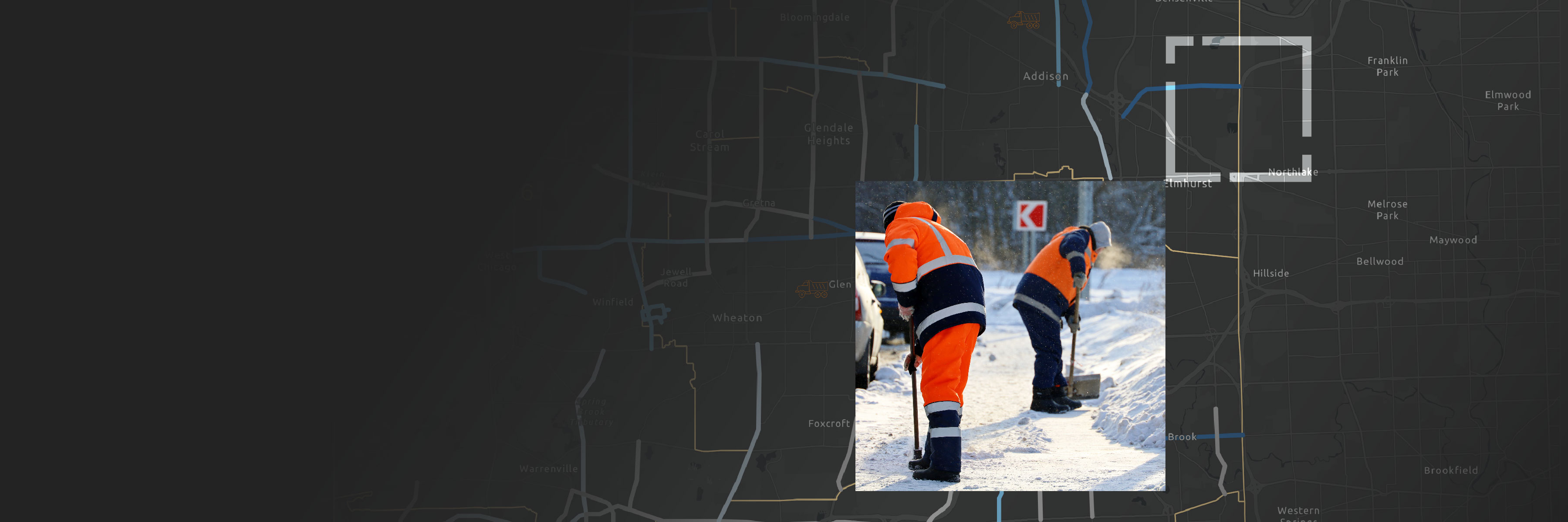 Two people in orange safety gear shoveling snow by a roadside with a background of a large dark gray map