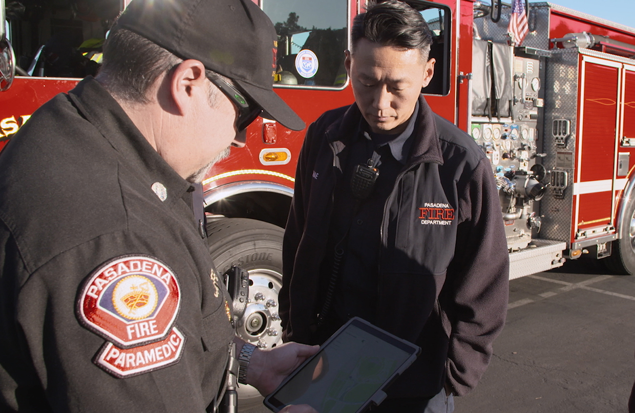 Two emergency response workers standing in front of a fire truck and looking at a map displayed on a tablet 